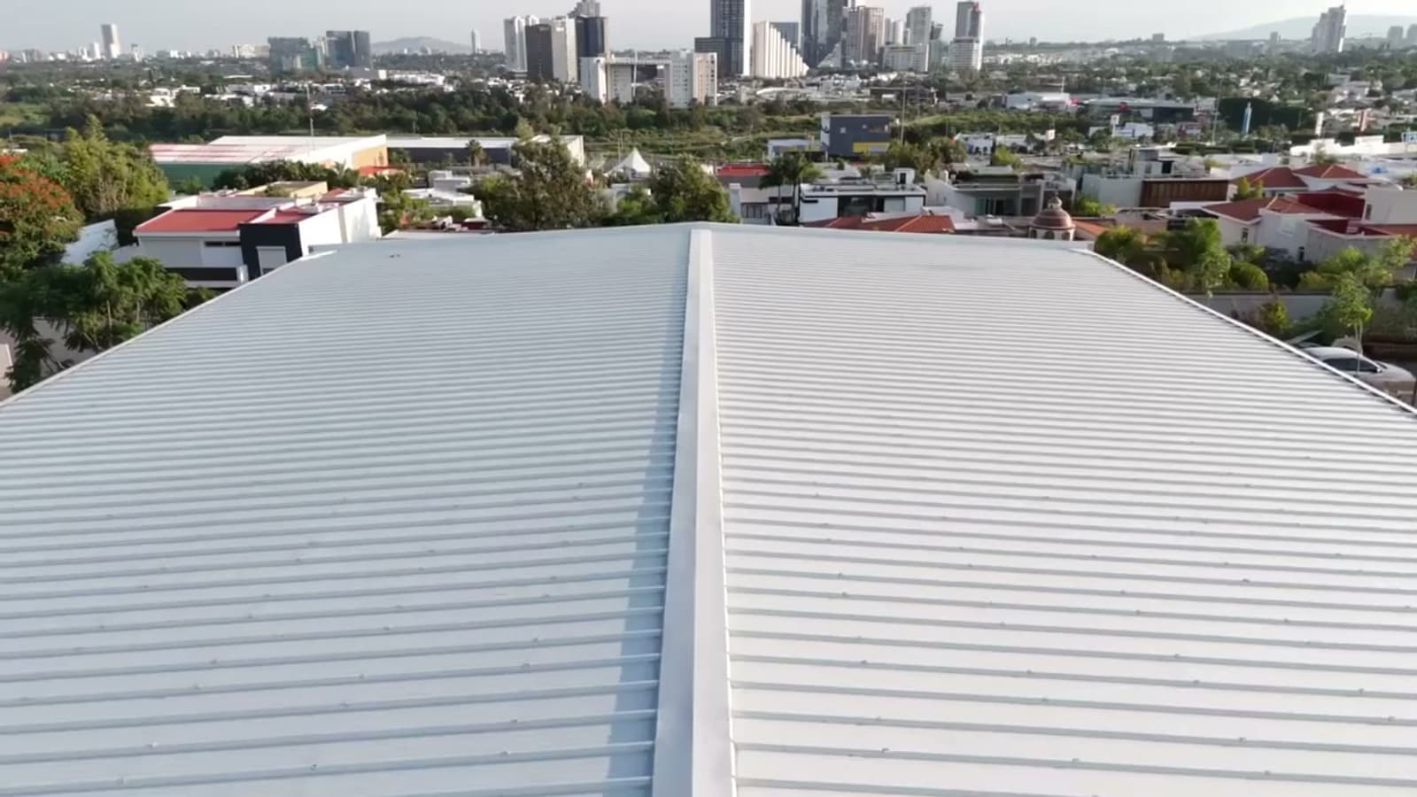 Vista aérea de la cubierta metálica del auditorio CECYTEJ, con la ciudad de Guadalajara al fondo